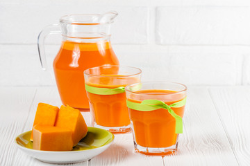 Pumpkin fresh juice in beautiful glasses and jug with pieces of ripe vegetable on white wooden background. Sweet orange juice. Healthy eating, diet theme. Close up photography. Horizontal banner