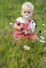 Portrait of a beautiful boy child sitting on summer green meadow with a teat in his mouth
