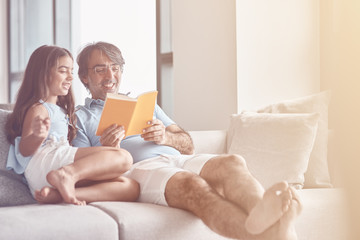 Cheerful father reading a book with his daughter