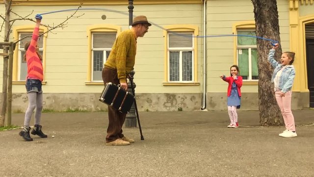 Old man jumping on a skipping rope with three girls in the street.