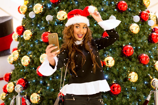 funny young Christmas girl taking selfie photo with mobile phone near Christmas tree