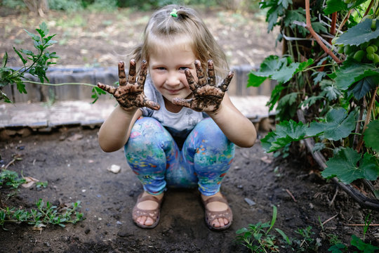 Little cute girl with dirty hands in the garden.