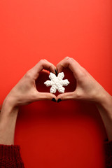 Christmas cookie white snowflake in female hands, on red background, hands in the shape of heart