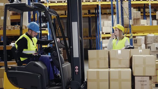 Young workers with smartphone and forklift in warehouse.