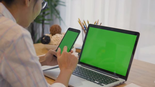4K: Over the shoulder shot of a woman typing on a computer laptop with a key-green