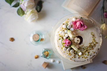Chiffon cake con cioccolato bianco decorata con pistacchi, meringhe e petali di rosa su tavolo di...