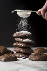 Dark chocolate chip cookies on a pile, sifting powdered sugar on the top.