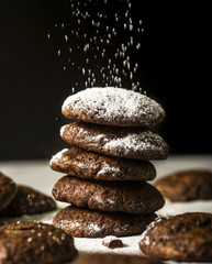 Dark chocolate chip cookies on a pile, sifting powdered sugar on the top.