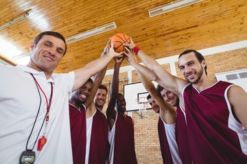 Players and coach holding basketball together in the court