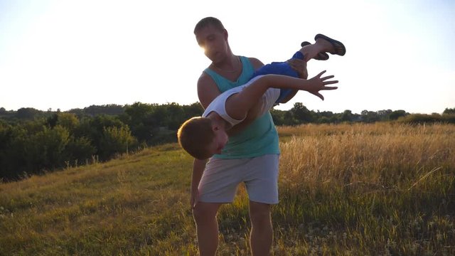 Father and son playing on the field at sunset. Happy daddy rotates his little child in hands. Boy imagines he flies like a plane. Happy family spending time outdoor. Active lifestyle. Slow motion