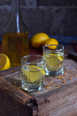 Homemade lemon tincture or ale on wooden background. Rustic style. Spice yellow liqueur in a glass. Alcohol drink.