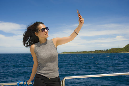 young attractive and happy Asian Chinese woman selfie portrait picture with mobile phone on boat or ferry smiling with blue sea background