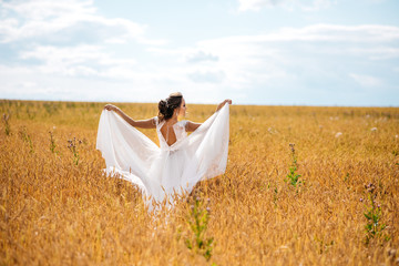 Fototapeta na wymiar Beautiful bride in wedding dress is dancing alone in a field of wheat and smile. View from the back