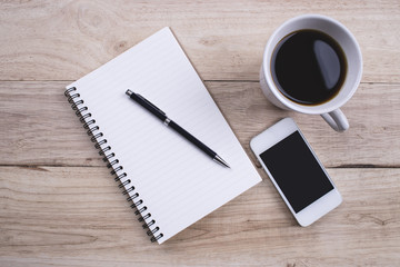 Top view Note book with pen and smartphone and a cup of coffee on wood table for Business