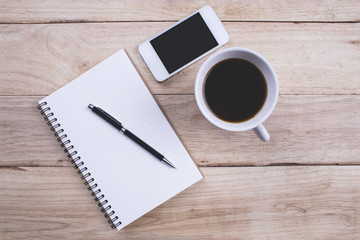 Top view Note book with pen and smartphone and a cup of coffee on wood table for Business