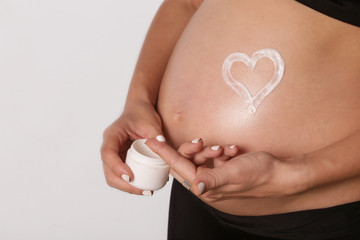 Pregnant woman applying moisturizer on belly, preventing pregnancy stretch marks