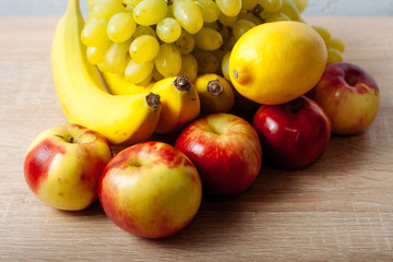 Bananas, apples, grapes and lemons on a wooden table.