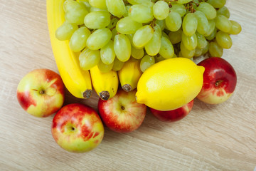Bananas, apples, grapes and lemons on a wooden table.