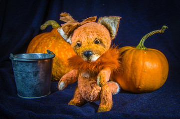 A fox-farmer's doll, next to a bucket and large orange pumpkins.