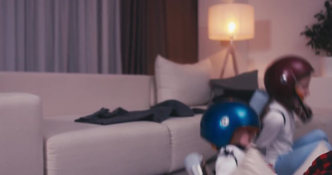 Funny cute dreamer siblings wearing helmets and rocket packs made from plastic bottles pretending to be astronauts, jumping from sofa. 4K UHD 60 FPS SLO MO