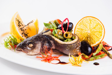 Baked sea bass with grilled green beans and olives on a white oval plate on a light background (close)