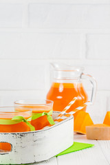 Pumpkin fresh juice in beautiful glasses and jug with pieces of ripe vegetable on white wooden background. Sweet orange juice. Healthy eating, diet theme. Close up photography. Vertical banner