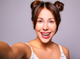 Naklejka premium Portrait of beautiful cute brunette woman model in casual clothes with no makeup making selfie photo on smartphone isolated on gray