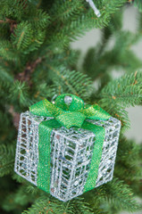 Silver color gift box with green ribbon on fir tree branch