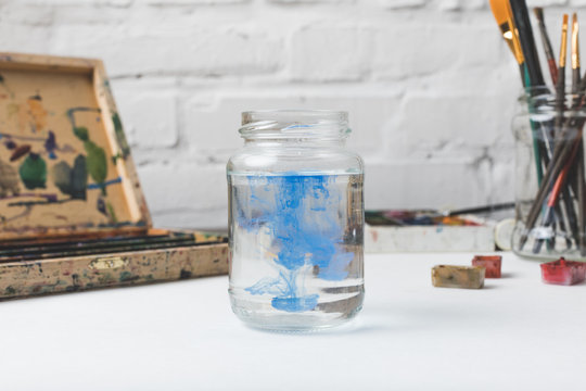 close-up view of glass jar with water and blue paint at designer workplace - Powered by Adobe