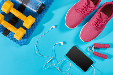 Flat lay shot of Sport equipment. Sneakers, water, earphones and phone on blue background.