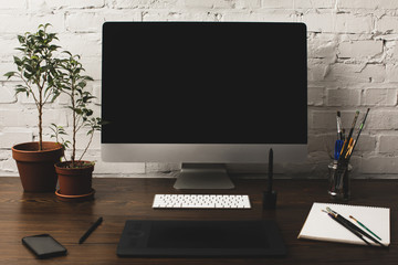 desktop computer with blank screen, graphics tablet and smartphone on wooden table
