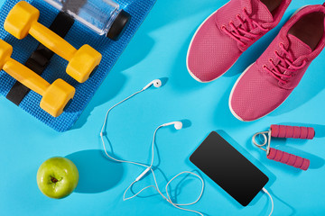 Flat lay shot of Sport equipment. Sneakers, water, earphones and phone on blue background.