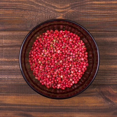 Pink pepper in a bowl on a wooden background