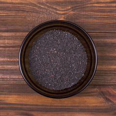Black sesame seeds in a bowl on a wooden background