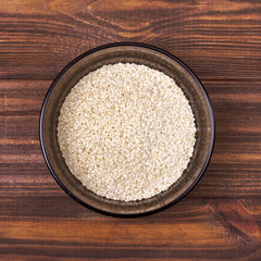 White sesame seeds in a bowl on a wooden background
