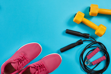 Athlete's set with female clothing, dumbbells and jump rope on bright blue background