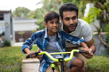 Obraz premium Father looking away while assisting son for cycling