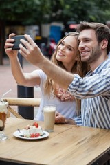 Cheerful couple holding smart phone while sitting at sidewalk