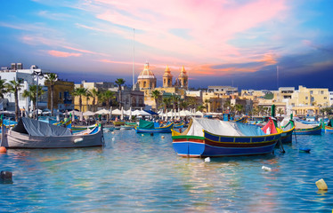 Cityscape and traditional boats in Marsaxlokk village harbor of Malta at dusk - obrazy, fototapety, plakaty