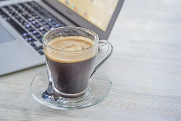Glass mug of hot coffee near the notebook on light background