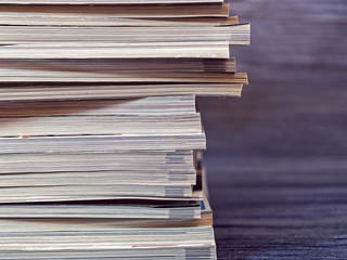 A stack of old magazines is on a dark background. Image on the topic of switching to digital storage media, recycling paper for recyclables and ecology