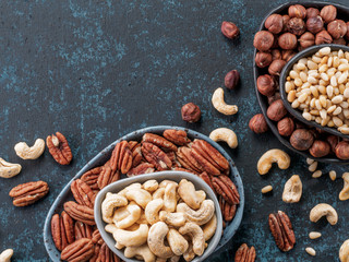 Background of nuts - cashew, pecan, pine nuts, hazelnuts - on dark blue background with copy space. Top view or flat lay