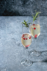 Two glasses of white champagne served with red berries and rosemary over blue texture background. Copy space