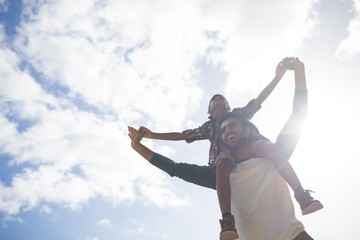 Low angle view of happy father carrying son on shoulder