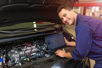 Mechanic Using Laptop While Examining Car Engine
