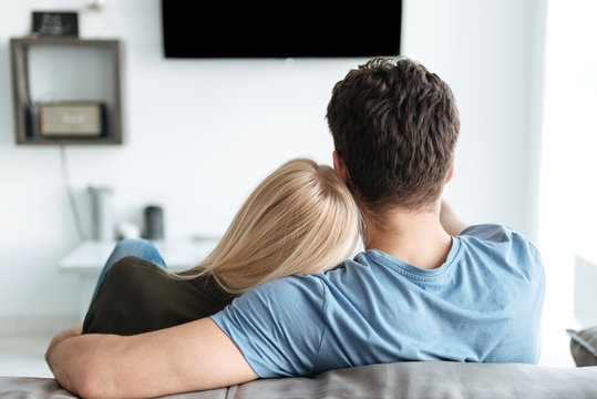 Back view of lovers sitting on sofa and watching TV