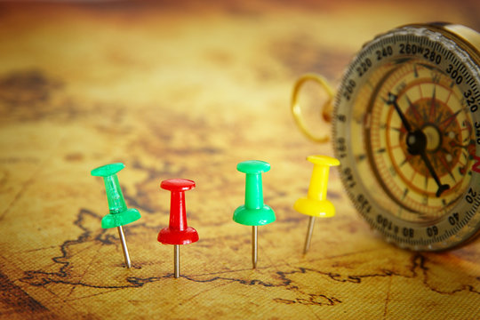 Image of pins attached to map, showing location or travel destination over old map next to vintage compass. selective focus.