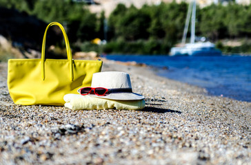 A hat, a beach bag, glasses and a towel lie on a beautiful coast. In the background is a large...