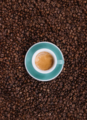 Delicious fresh morning espresso with a beautiful crema in a ceramic green cup with a saucer on the coffee beans background, top view