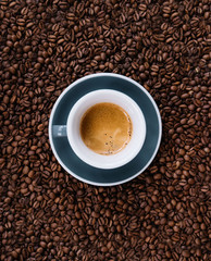 Delicious fresh morning espresso with a beautiful crema in a ceramic grey cup with a saucer on the coffee beans background, top view